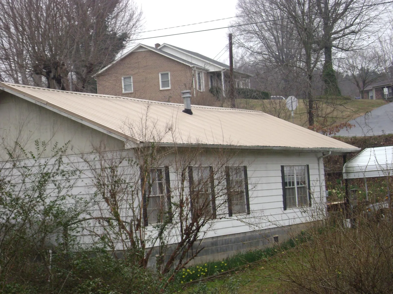 Tan metal roof on a white sided house set into a hillside — Commercial Roofing by Roofing Brothers in Irvine